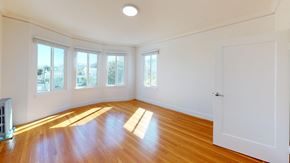 San Francisco apartment for rent - A room with wooden floors and white walls has a white door and a window with a view of trees.