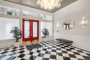 San Francisco apartment for rent - Grand entrance to a building, featuring a double door with a handle, a chandelier hangs from the ceiling, and two plotted plants, one on each side of the door