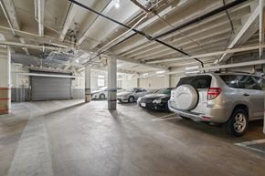 San Francisco apartment for rent - Underground parking garage with cars, marked spaces, lighting, and visible piping; closed shutter door