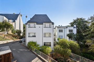 Berkeley apartment for rent - A white building with a black roof is surrounded by greenery and a clear blue sky.