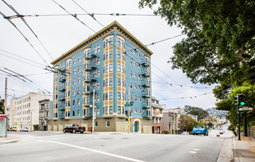 San Francisco apartment for rent - A blue and yellow building is situated on a street corner with cars parked on the side of the road.