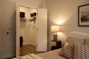 Biddeford apartment for rent - A bedroom with a bed, a nightstand with a lamp, and a closet with clothes hanging.