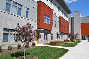 Rochester apartment for rent - A modern building with a red and grey facade and a green lawn in front.