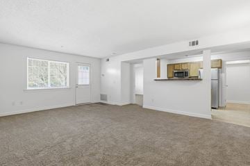 Savannah apartment for rent - A spacious living room with a carpeted floor and a kitchenette in the background.