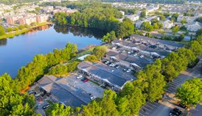 Statesboro apartment for rent - A parking lot is surrounded by trees and a body of water.