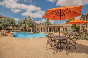 San Antonio apartment for rent - A large orange umbrella is in the foreground of a pool area at The Villages at Lost Creek Apartments, San Antonio, TX, 78247