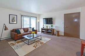 Evansville apartment for rent - A living room with a brown couch, a coffee table, and a flat screen TV mounted on the wall.