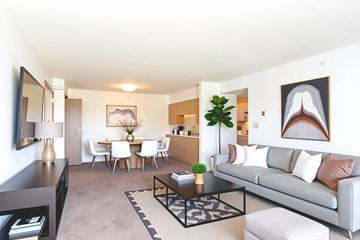 Evansville apartment for rent - A living room with a grey couch, a coffee table, a dining table with chairs, and a potted plant.