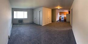 Sayville apartment for rent - an empty living room with a kitchen in the background at Brookwood at Sayville, Sayville, NY, 11782