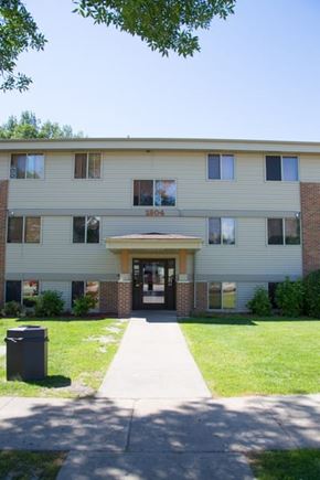Grand Forks apartment for rent - A building with a brown door and windows with trees in the background.