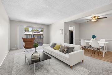 Los Angeles apartment for rent - A living room with a white couch, a brown chair, and a glass table with a plant on it.
