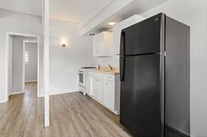 Los Angeles apartment for rent - A black refrigerator stands in a kitchen with white cabinets and a wooden floor.