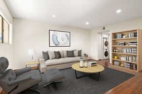 Canoga Park apartment for rent - A living room with a grey couch, a grey chair, a black coffee table, a lamp, a book, a plant, a picture on the wall, a white door, and a bookshelf.