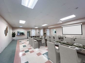 A conference room with tables and chairs and a projection screen on the wall