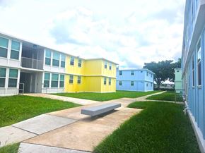 Ft Lauderdale apartment for rent - A building with a blue and yellow exterior is surrounded by a grassy area and a concrete walkway.