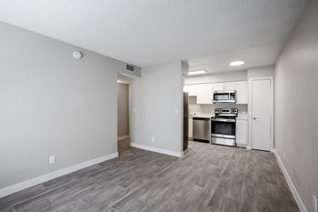 An empty living room with a kitchen in the background