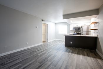 An empty living room with a kitchen in the background