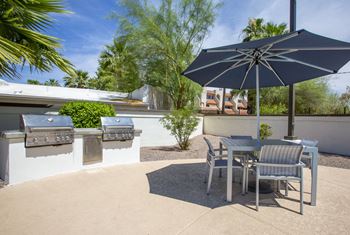 A patio with two bbq grills and a table with chairs and an umbrella