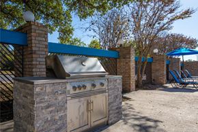 San Antonio apartment for rent - A stone BBQ grill with a blue awning and chairs in the background.