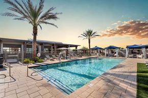 Mesa apartment for rent - A large swimming pool surrounded by a patio area with lounge chairs and umbrellas.