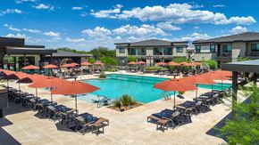Tucson apartment for rent - A pool surrounded by chairs and umbrellas with apartment buildings in the background.