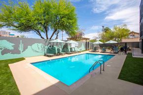 Tucson apartment for rent - A large outdoor swimming pool surrounded by a concrete deck and a green tree.