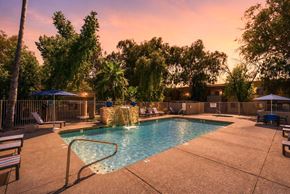 Glendale apartment for rent - A pool surrounded by trees and chairs with a sunset in the background.