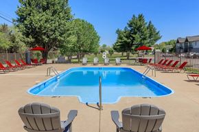 Murfreesboro apartment for rent - A large blue swimming pool surrounded by red chairs and umbrellas.