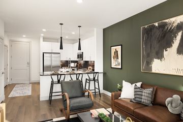 Northglenn apartment for rent - A modern living room with a brown leather couch and a kitchen area in the background.