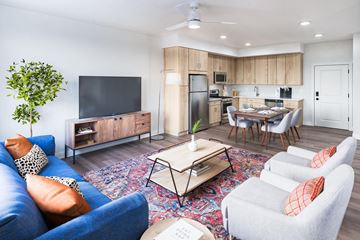 Cottage Grove apartment for rent - A living room with a blue couch, a wooden cabinet, a television, a dining table with chairs, and a potted plant.