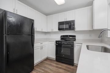 Plainfield apartment for rent - A black refrigerator is in a kitchen with white cabinets and a black stove.