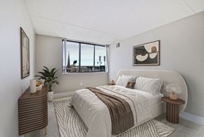 Detroit apartment for rent - A bedroom with a large bed and a window overlooking a cityscape.