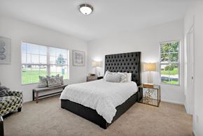 East Lansing apartment for rent - A bedroom with a large bed and a bench in front of a window.