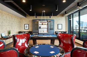 Minneapolis apartment for rent - A poker table surrounded by red chairs in a room with a pool table and a view of the city.