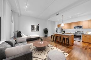 Detroit apartment for rent - A modern living room with a grey couch, a coffee table, and a kitchen area in the background.