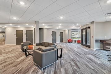 Lansing apartment for rent - A spacious office lounge with grey couches and wooden flooring.