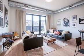 Pittsburgh apartment for rent - A living room with a black couch, a brown rug, and a wooden floor.