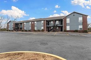 Rogers apartment for rent - A large grey building with a parking lot in front.