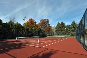 New Hudson apartment for rent - A red tennis court surrounded by trees and a fence.