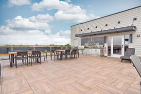 Troy apartment for rent - A patio with wooden tables and chairs is in front of a building.