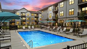 Mcmurray apartment for rent - A swimming pool surrounded by lounge chairs and umbrellas in front of a building.