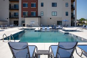 Rogers apartment for rent - A pool surrounded by chairs and tables in front of a building.