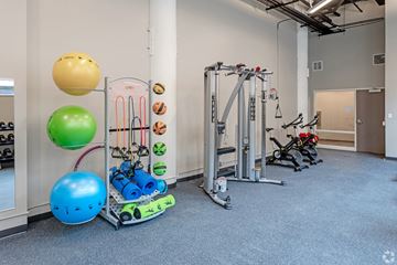 St. Paul apartment for rent - A gym with a variety of equipment including a leg press machine, a rowing machine, and a TRX suspension trainer.