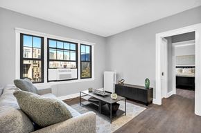 Cleveland apartment for rent - A living room with a grey couch, a coffee table, and a large window with a view of a building.