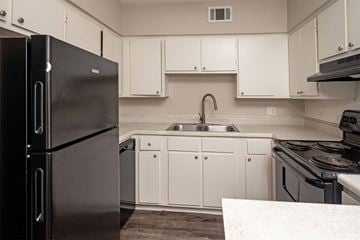 Little Rock apartment for rent - A black refrigerator stands in a kitchen with white cabinets and a sink.