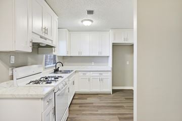 Tustin apartment for rent - A kitchen with white cabinets and a white stove top oven.