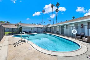 Redlands apartment for rent - A pool surrounded by a black fence with a chair and palm trees in the background.