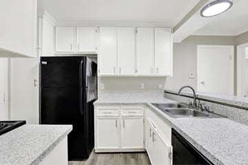Fullerton apartment for rent - A black refrigerator sits in a kitchen with white cabinets and a granite countertop.