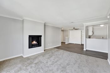 A living room with a fireplace and a kitchen area in the background.