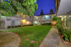 Orange apartment for rent - A well-lit apartment complex with a green lawn and trees.